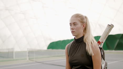 TRACKING-Young-Caucasian-female-tennis-player-entering-the-court,-rackets-in-a-backpack.-4K-UHD-RAW-graded-footage